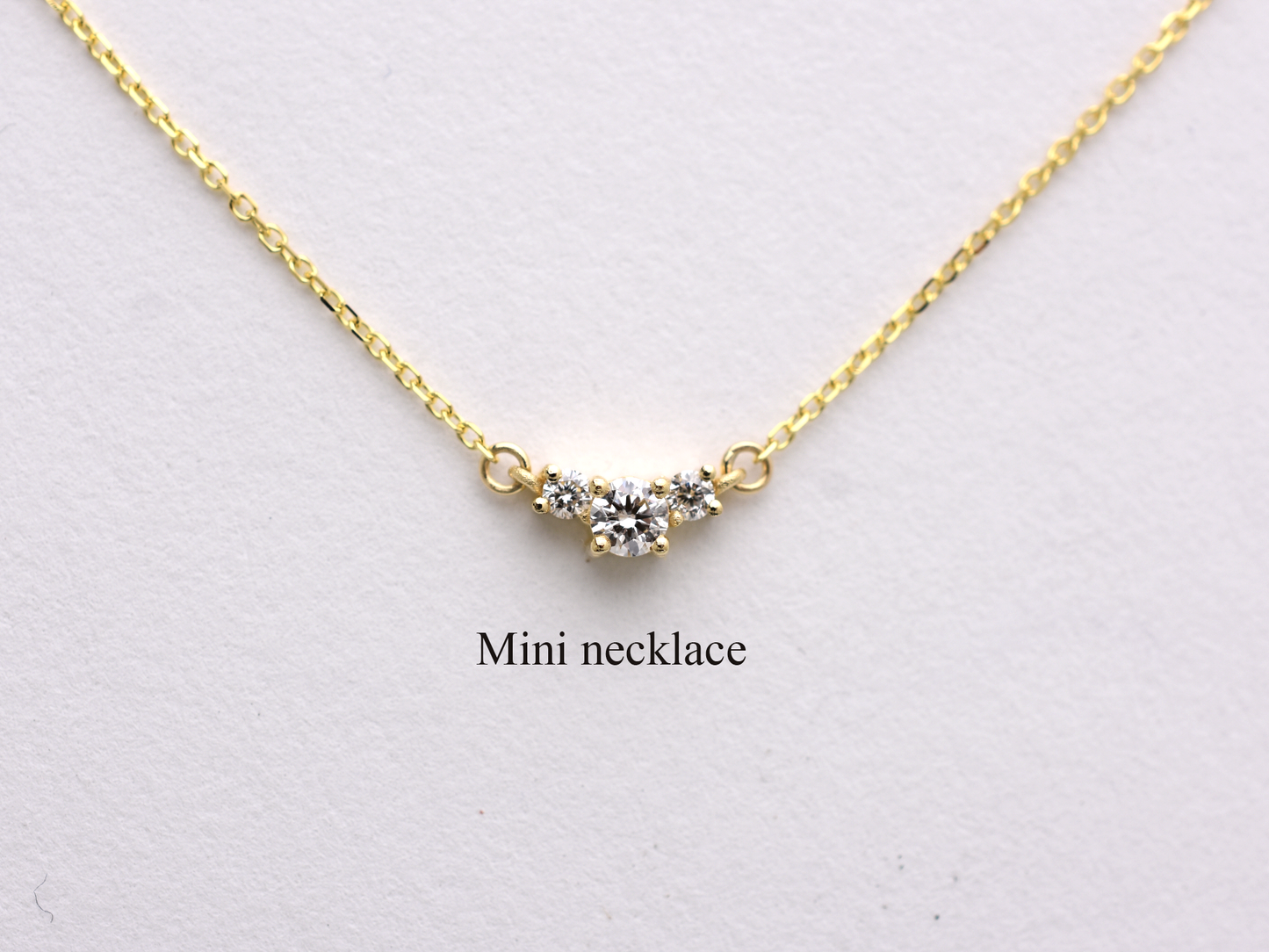 featuring a dainty three-stone diamond cluster pendant. The centerpiece consists of one slightly larger round brilliant cut stone flanked by two smaller stones in a minimalist prong setting on a fine gold cable chain with a lobster claw clasp