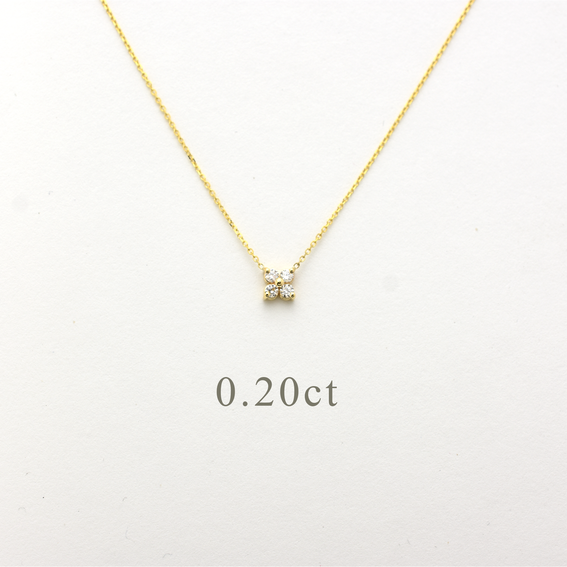 Close-up of a delicate 14K yellow gold chain necklace featuring a small, clover-shaped cluster pendant. The pendant consists of four brilliant round-cut diamonds totaling 0.20 carats, set closely together to create a tiny floral design. The necklace is displayed on a white background.