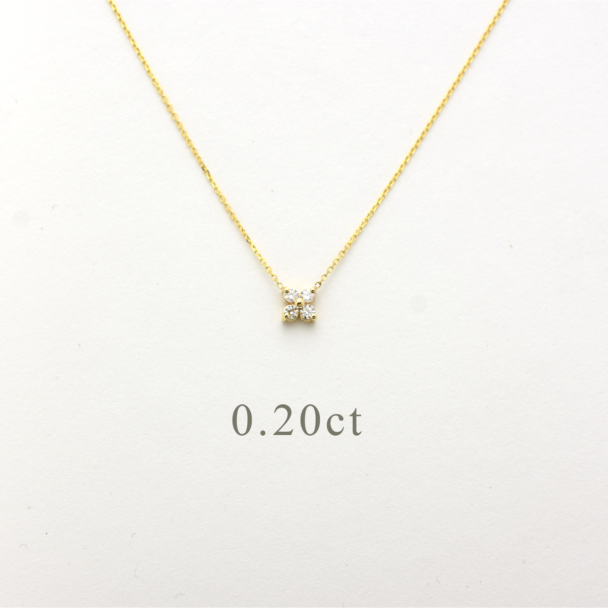 Close-up of a delicate 14K yellow gold chain necklace featuring a small, clover-shaped cluster pendant. The pendant consists of four brilliant round-cut diamonds totaling 0.20 carats, set closely together to create a tiny floral design. The necklace is displayed on a white background.