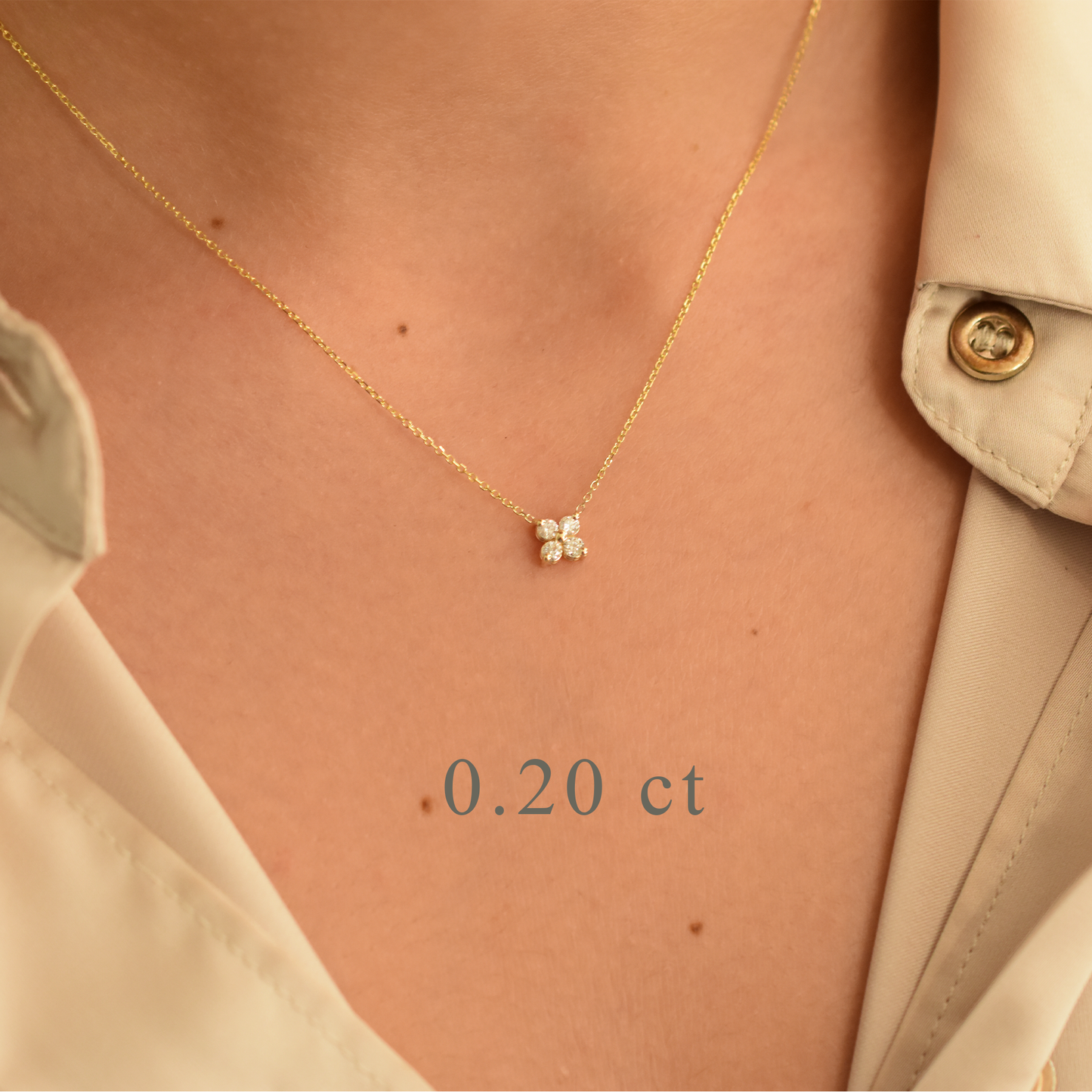 Gold necklace with a diamond pendant on a person wearing a beige outfit.