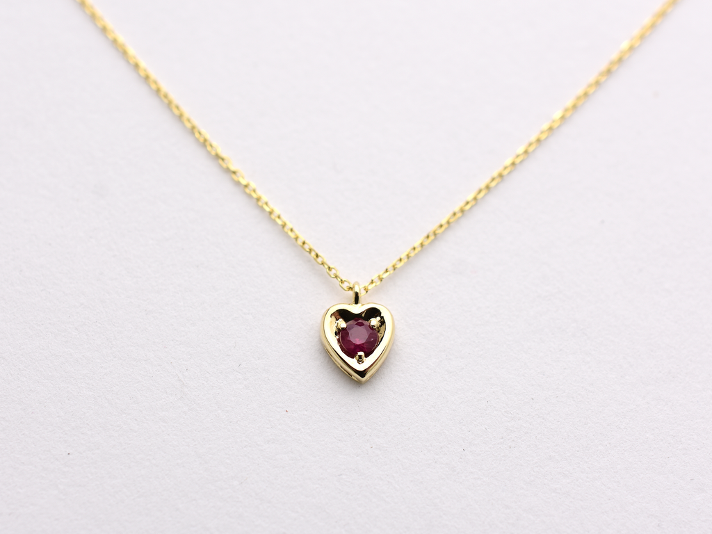 14k gold heart shaped necklace minimalistic design . in the center is a 3 mm natural red ruby , the chain is a 0.8mm dainty cable link chain displayed on a white background