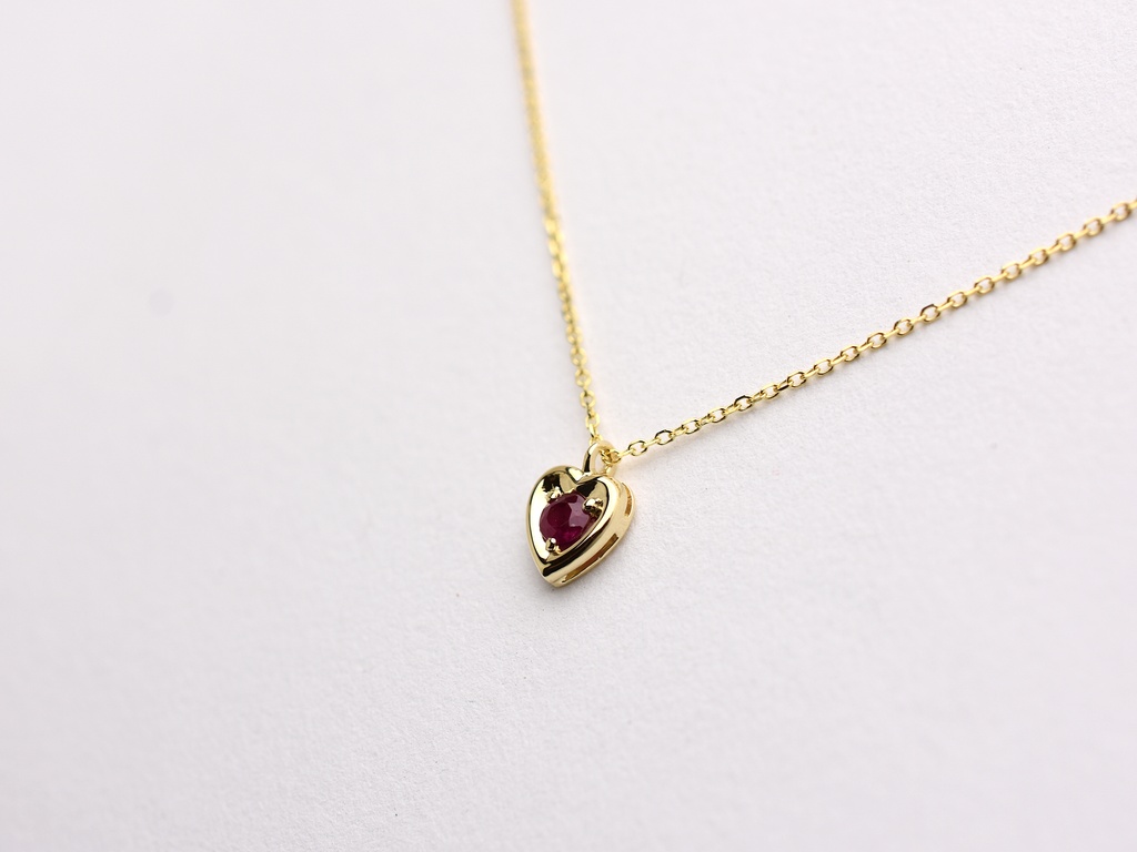 14k gold heart shaped necklace minimalistic design . in the center is a 3 mm natural red ruby , the chain is a 0.8mm dainty cable link chain displayed on a white background