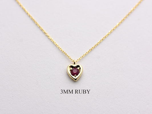 14k gold heart shaped necklace minimalistic design . in the center is a 3 mm natural red ruby , the chain is a 0.8mm dainty cable link chain displayed on a white background