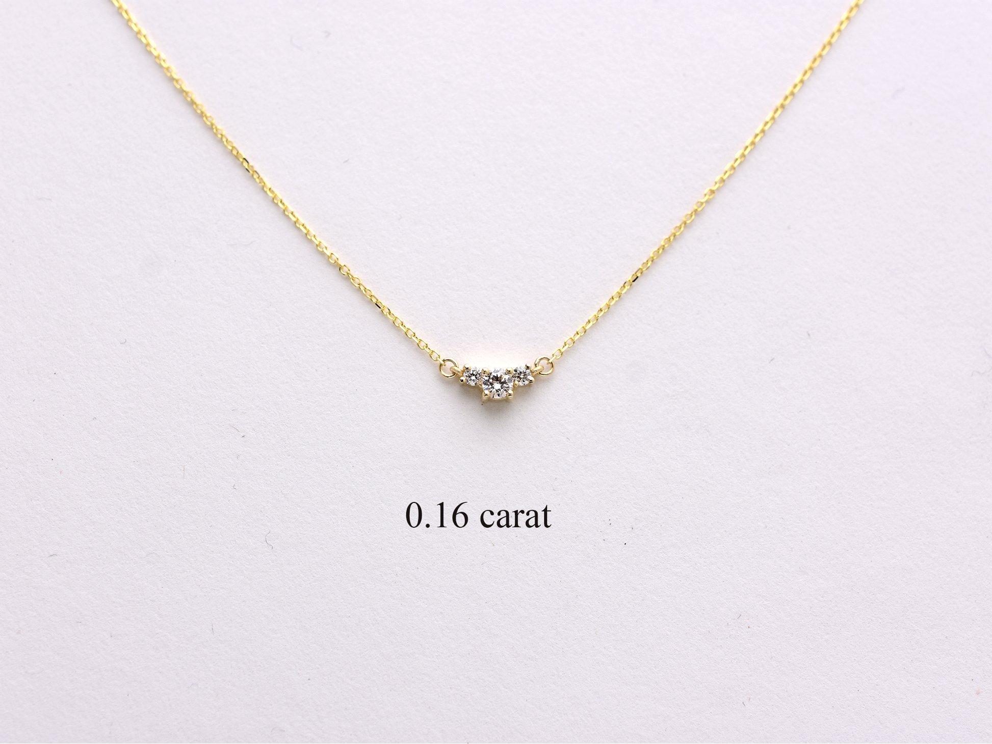  featuring a dainty three-stone diamond cluster pendant. The centerpiece consists of one slightly larger round brilliant cut stone flanked by two smaller stones in a minimalist prong setting on a fine gold cable chain with a lobster claw clasp