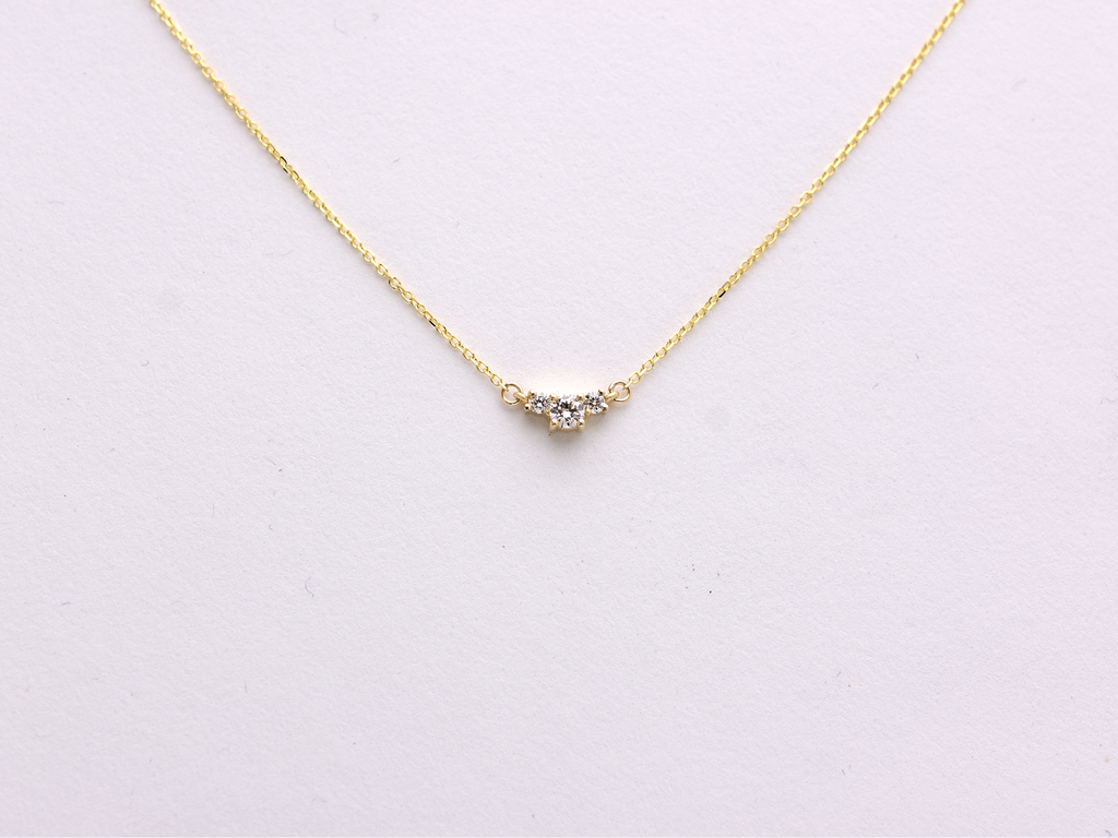  featuring a dainty three-stone diamond cluster pendant. The centerpiece consists of one slightly larger round brilliant cut stone flanked by two smaller stones in a minimalist prong setting on a fine gold cable chain with a lobster claw clasp