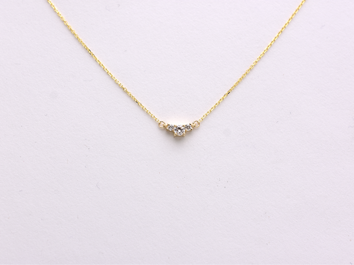  featuring a dainty three-stone diamond cluster pendant. The centerpiece consists of one slightly larger round brilliant cut stone flanked by two smaller stones in a minimalist prong setting on a fine gold cable chain with a lobster claw clasp