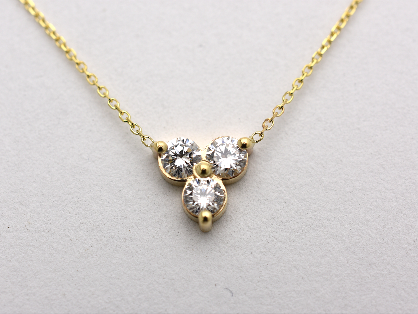 close up 14k yellow gold necklace with a three-stone pendant of round brilliant cut 0.60  carat diamonds  on a white background