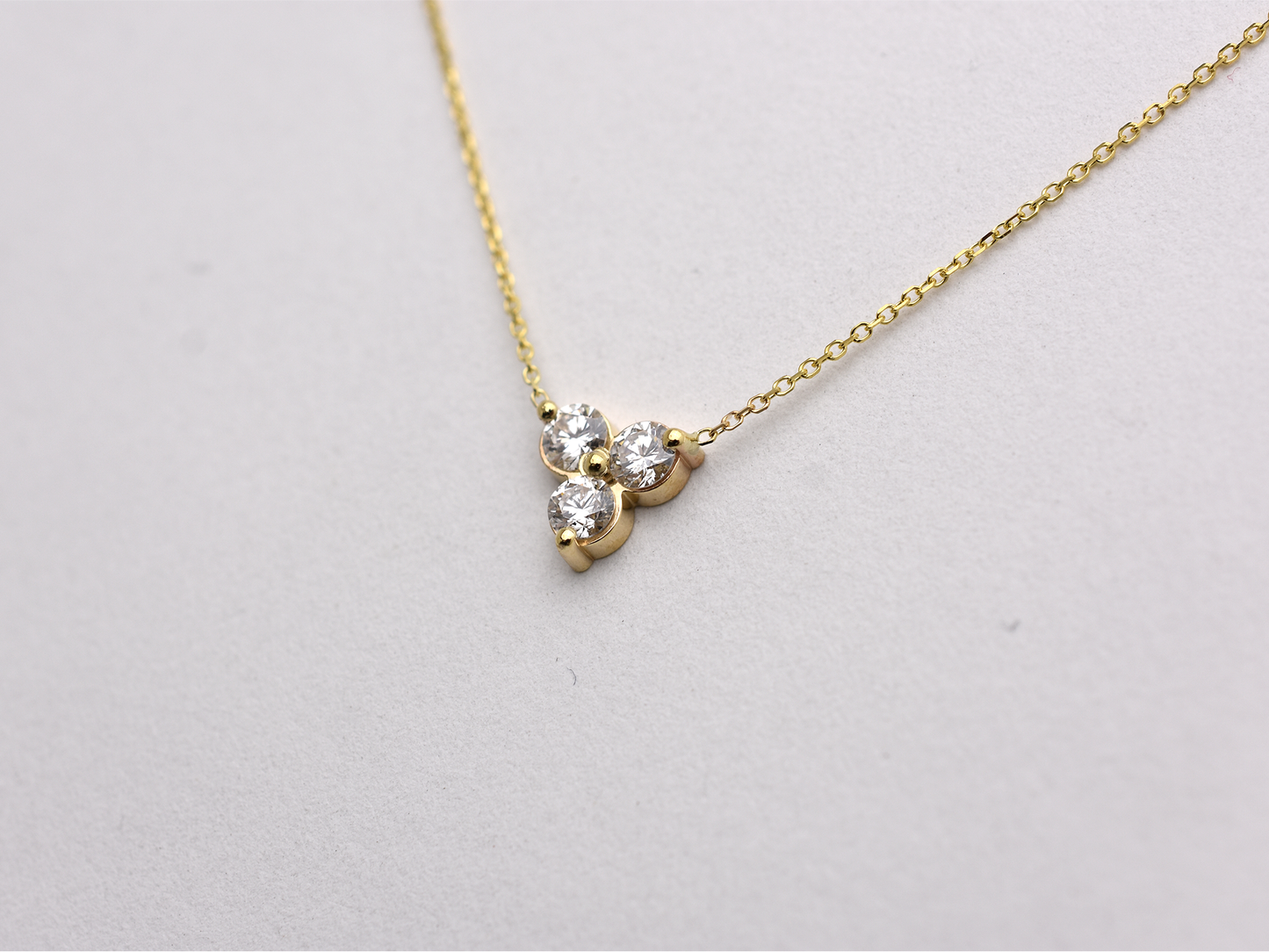 side view 14k yellow gold necklace with a three-stone pendant of round brilliant cut 0.60  carat diamonds  on a white background