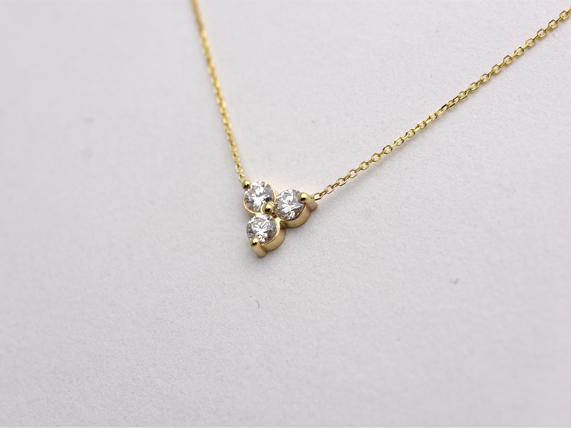 side view 14k yellow gold necklace with a three-stone pendant of round brilliant cut 0.60  carat diamonds  on a white background