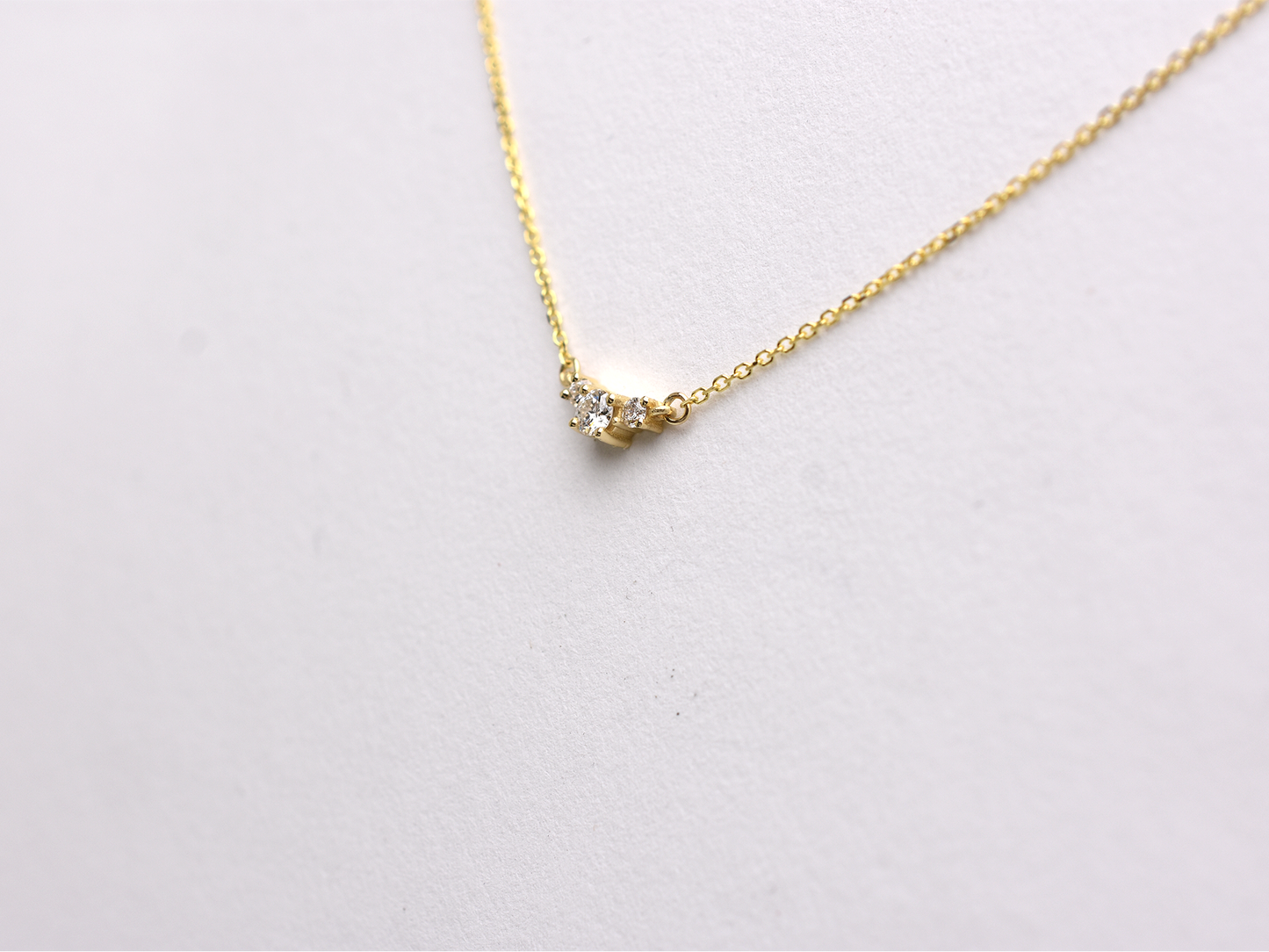  featuring a dainty three-stone diamond cluster pendant. The centerpiece consists of one slightly larger round brilliant cut stone flanked by two smaller stones in a minimalist prong setting on a fine gold cable chain with a lobster claw clasp