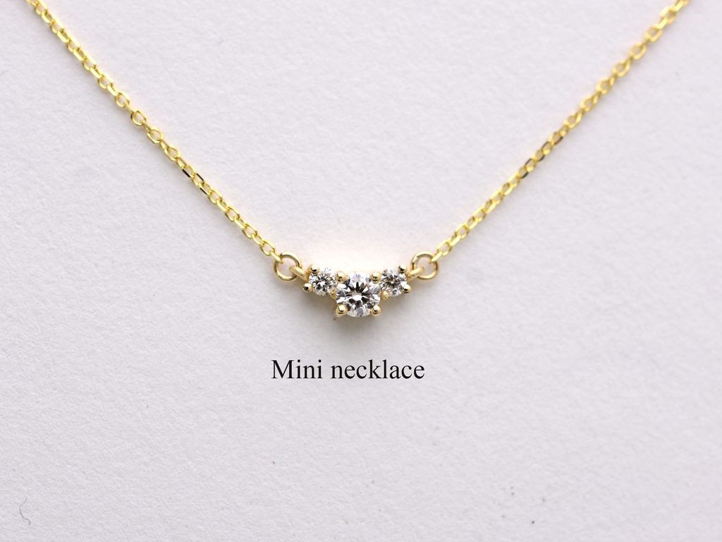  featuring a dainty three-stone diamond cluster pendant. The centerpiece consists of one slightly larger round brilliant cut stone flanked by two smaller stones in a minimalist prong setting on a fine gold cable chain with a lobster claw clasp