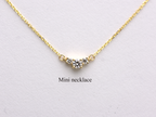  featuring a dainty three-stone diamond cluster pendant. The centerpiece consists of one slightly larger round brilliant cut stone flanked by two smaller stones in a minimalist prong setting on a fine gold cable chain with a lobster claw clasp