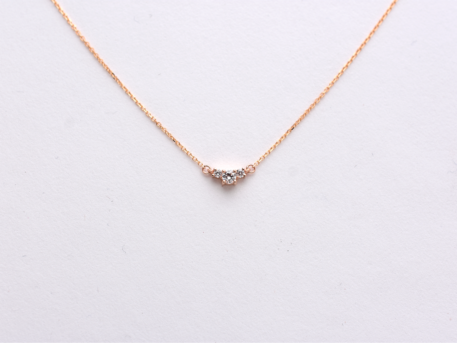  featuring a dainty three-stone diamond cluster pendant. The centerpiece consists of one slightly larger round brilliant cut stone flanked by two smaller stones in a minimalist prong setting on a fine gold cable chain with a lobster claw clasp