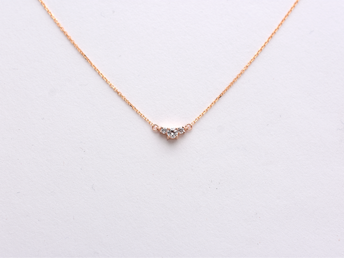  featuring a dainty three-stone diamond cluster pendant. The centerpiece consists of one slightly larger round brilliant cut stone flanked by two smaller stones in a minimalist prong setting on a fine gold cable chain with a lobster claw clasp