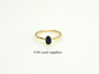 A minimalist 14k yellow gold solitaire ring featuring a 0.60 carat oval-cut deep blue sapphire. The gemstone is secured in a smooth bezel setting on a slim, polished gold band, centered against a clean white background with a soft reflection.