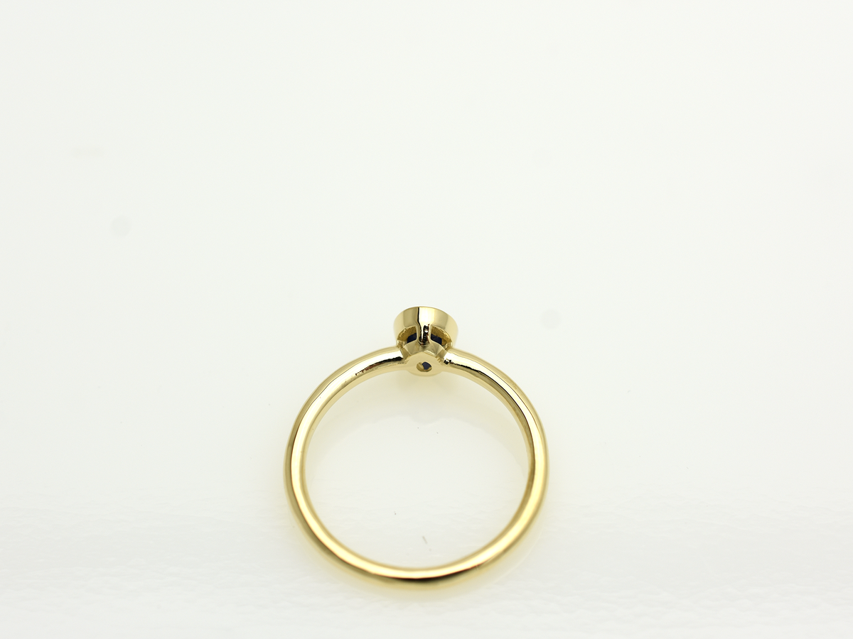 A minimalist 14k yellow gold solitaire ring featuring a 0.60 carat oval-cut deep blue sapphire. The gemstone is secured in a smooth bezel setting on a slim, polished gold band, centered against a clean white background with a soft reflection.