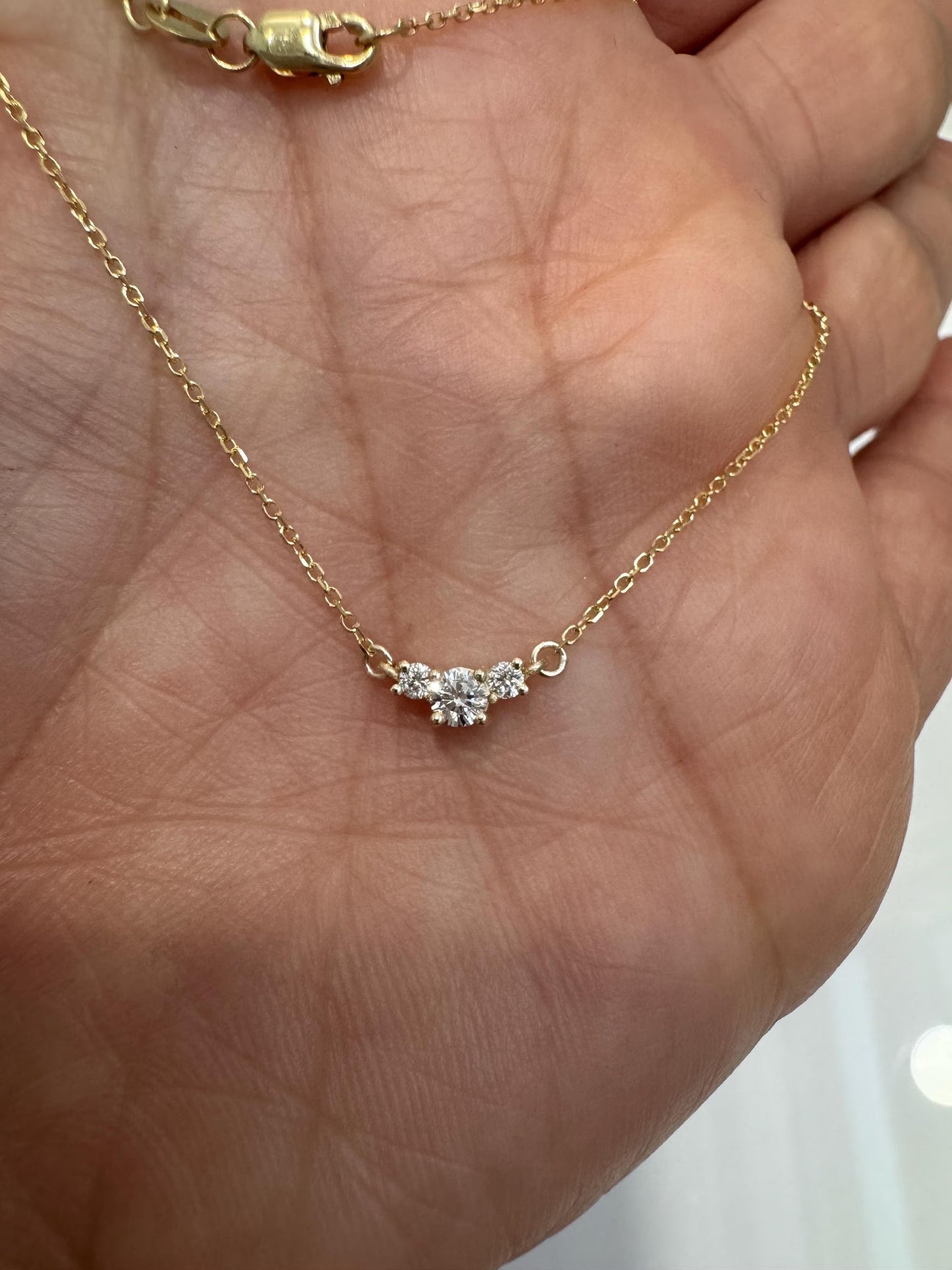 Gold necklace with a diamond pendant held in a hand against a neutral background