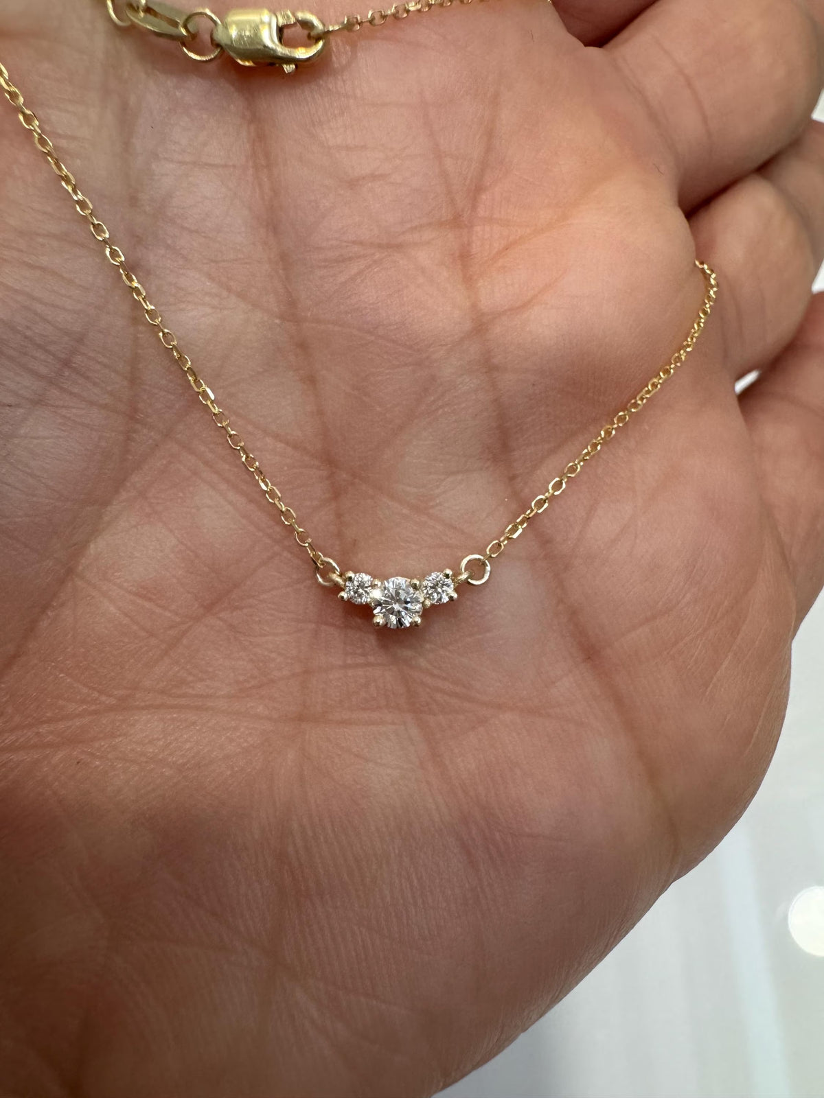 Gold necklace with a diamond pendant held in a hand against a neutral background
