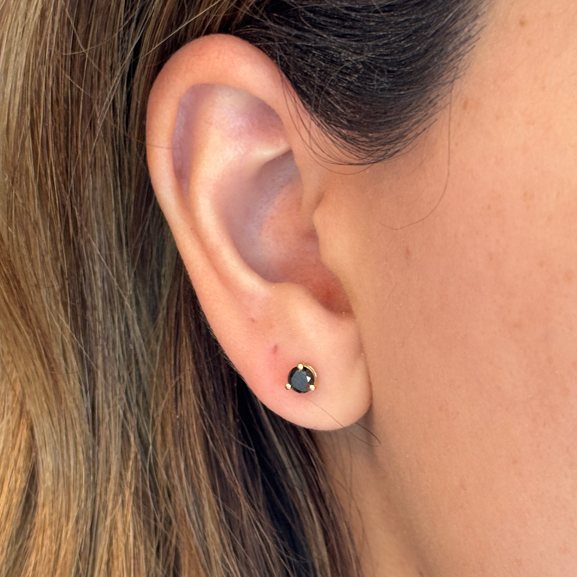 Close-up of an ear wearing a black stud earring with hair partially obscuring the view.