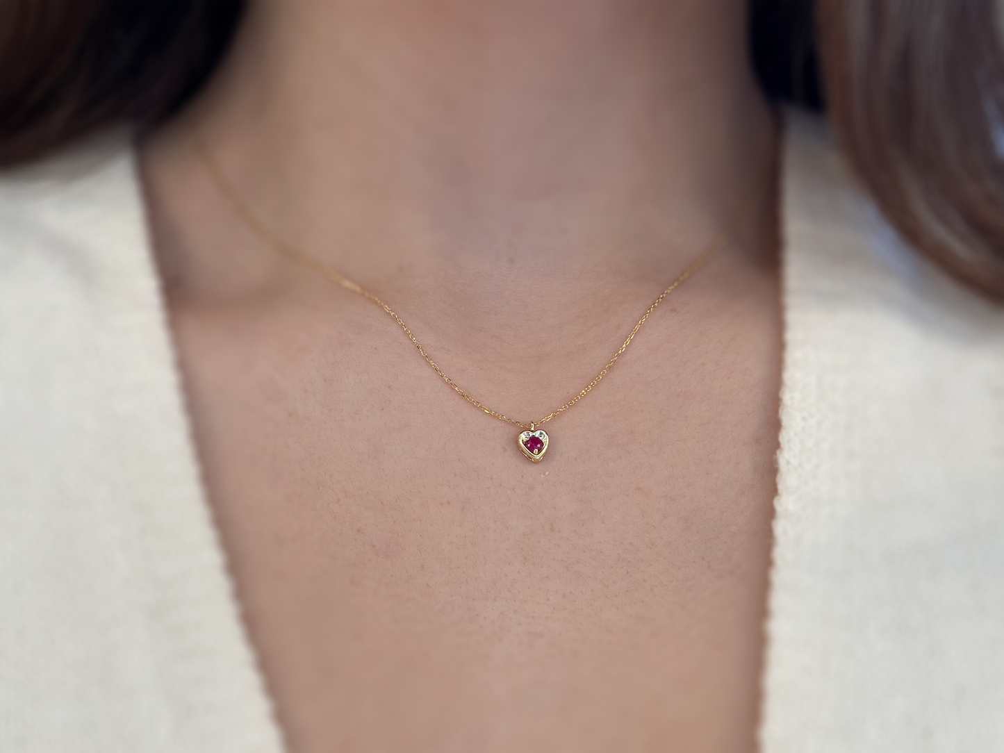 14k gold heart shaped necklace minimalistic design . in the center is a 3 mm natural red ruby , the chain is a 0.8mm dainty cable link chain displayed on a white background