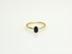 A minimalist 14k yellow gold solitaire ring featuring a 0.60 carat oval-cut deep blue sapphire. The gemstone is secured in a smooth bezel setting on a slim, polished gold band, centered against a clean white background with a soft reflection.