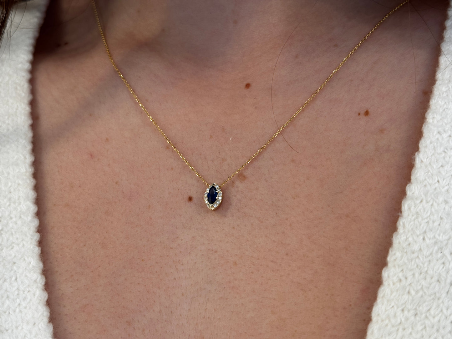  14K gold necklace featuring a marquise-cut sapphire center stone surrounded by a delicate diamond halo displayed on a model