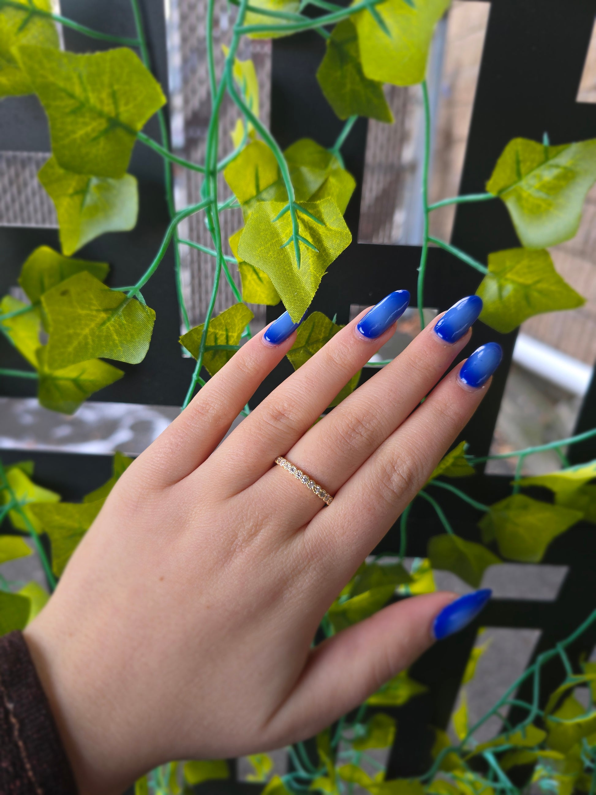 14k yellow gold dainty wedding band featuring a row of round diamonds. Each diamond is set in a scalloped bezel with fine milgrain beaded edges. The ring is shown on a reflective white surface, highlighting the warm gold tones and sparkling stones.
