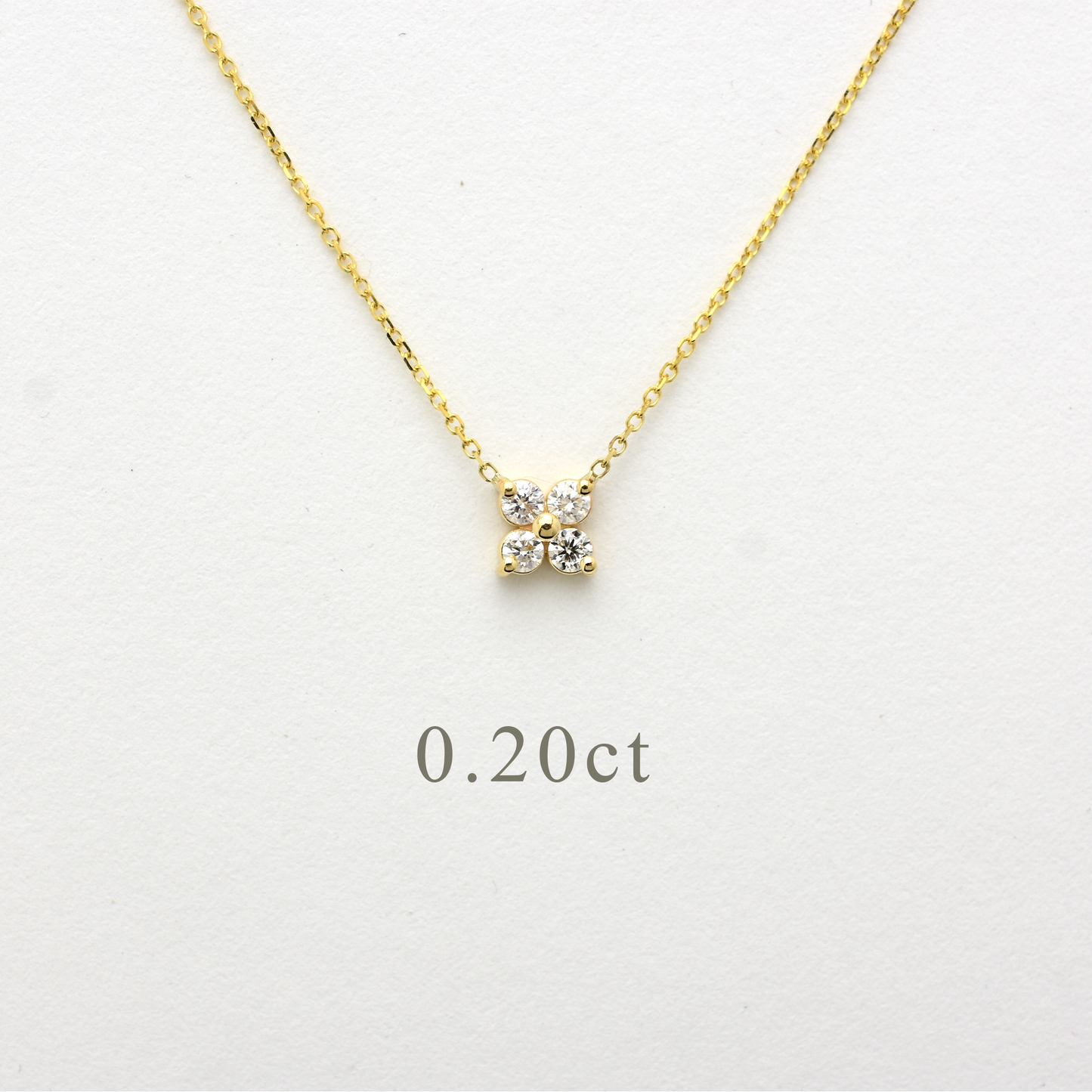 Close-up of a delicate 14K yellow gold chain necklace featuring a small, clover-shaped cluster pendant. The pendant consists of four brilliant round-cut diamonds totaling 0.20 carats, set closely together to create a tiny floral design. The necklace is displayed on a white background.