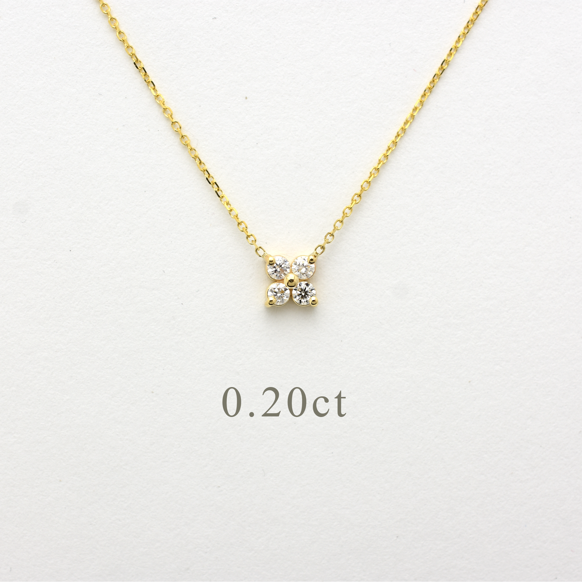 Close-up of a delicate 14K yellow gold chain necklace featuring a small, clover-shaped cluster pendant. The pendant consists of four brilliant round-cut diamonds totaling 0.20 carats, set closely together to create a tiny floral design. The necklace is displayed on a white background.