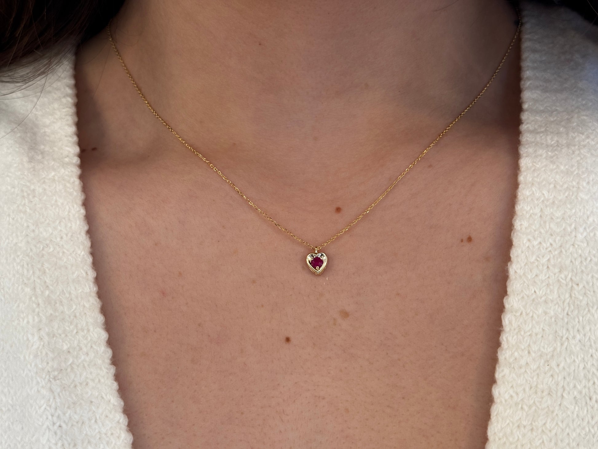 14k gold heart shaped necklace minimalistic design . in the center is a 3 mm natural red ruby , the chain is a 0.8mm dainty cable link chain 