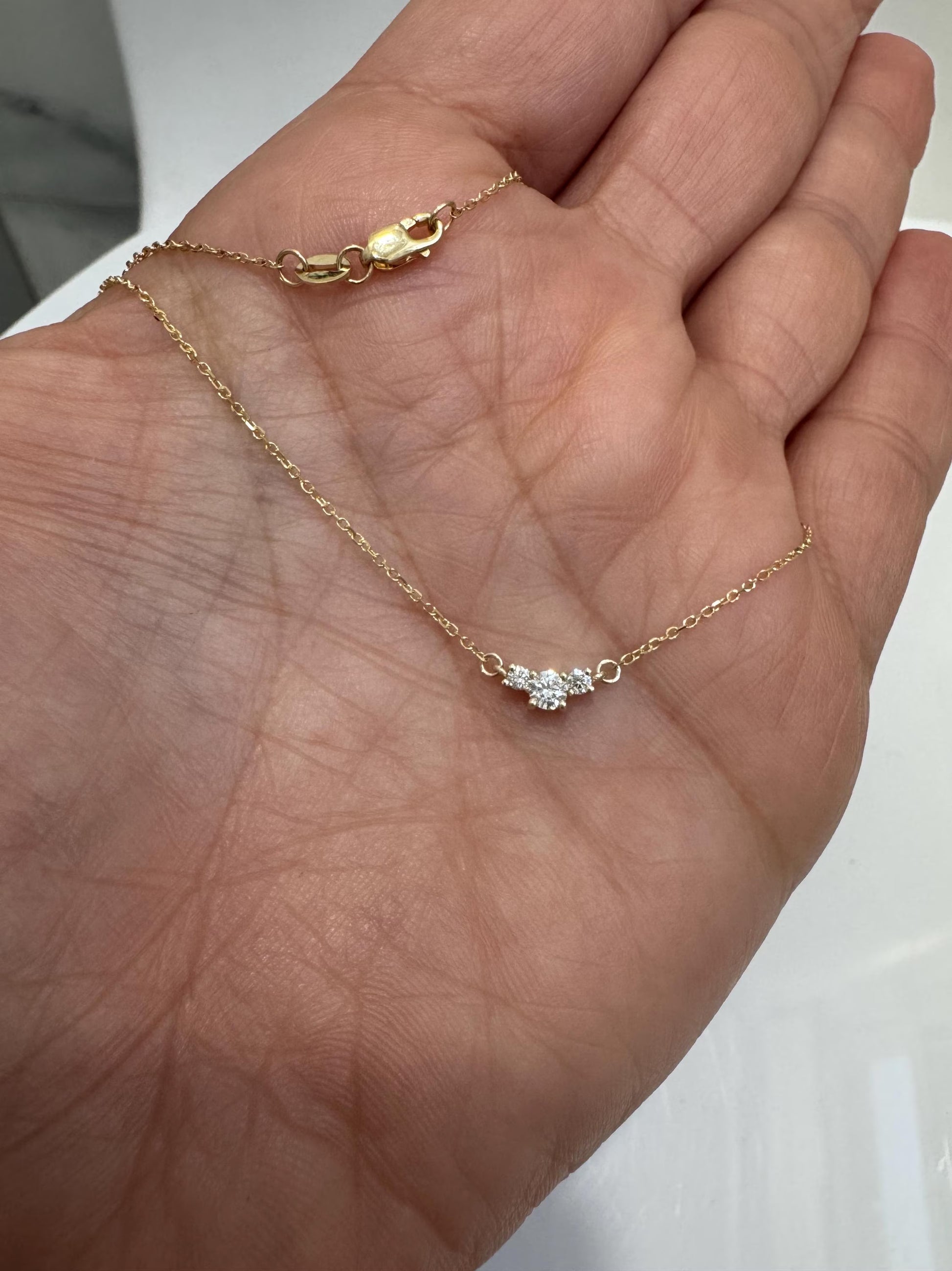 Gold necklace with a small diamond pendant held in a hand against a neutral background