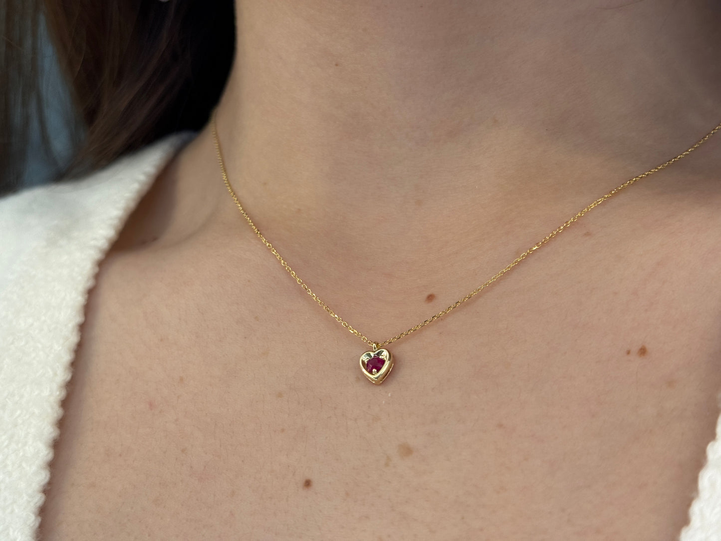 14k gold heart shaped necklace minimalistic design . in the center is a 3 mm natural red ruby , the chain is a 0.8mm dainty cable link chain displayed on a white background