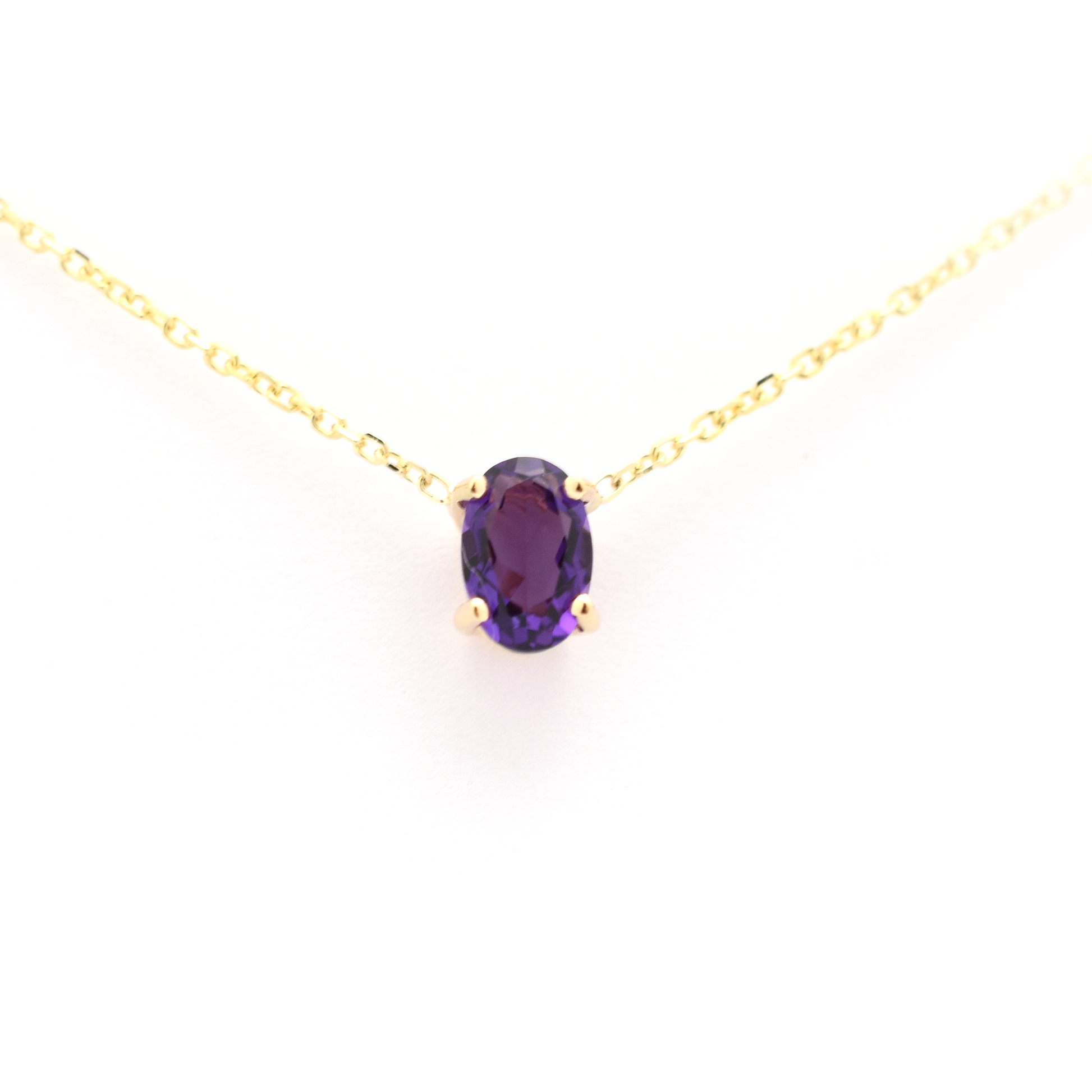 A 14 k gold necklace with a natural oval Amethyst gemstone prong set on it, displayed against a white background.