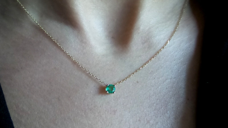 14k gold natural round shaped emerald set in a 4 prong setting with a delicate chain floating 